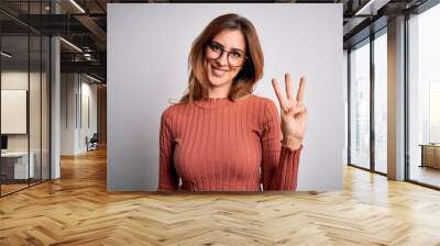 Young beautiful brunette woman wearing casual sweater and glasses over white background showing and pointing up with fingers number three while smiling confident and happy. Wall mural