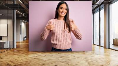 Young beautiful brunette woman wearing casual sweater over isolated pink background success sign doing positive gesture with hand, thumbs up smiling and happy. Cheerful expression and winner gesture. Wall mural