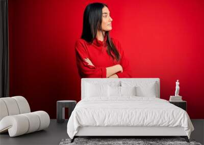 Young beautiful brunette woman wearing casual sweater over isolated red background looking to the side with arms crossed convinced and confident Wall mural