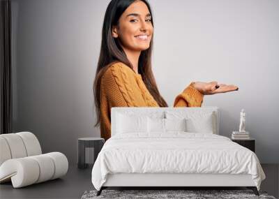 Young beautiful brunette woman wearing casual sweater over isolated white background pointing aside with hands open palms showing copy space, presenting advertisement smiling excited happy Wall mural