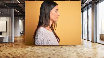 Young beautiful brunette woman wearing white casual sweater over yellow background looking to side, relax profile pose with natural face with confident smile. Wall mural