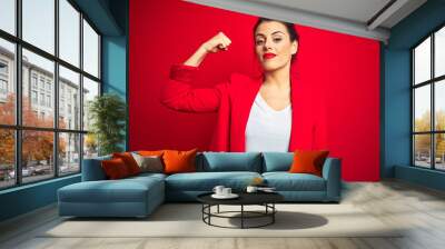 Young beautiful business woman standing over red isolated background Strong person showing arm muscle, confident and proud of power Wall mural