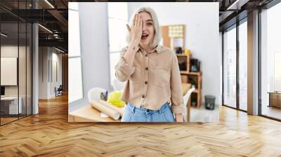 Young beautiful caucasian woman at construction office covering one eye with hand, confident smile on face and surprise emotion. Wall mural