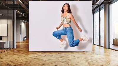 Young beautiful chinese girl wearing casual clothes and sunglasses smiling happy. Jumping with smile on face over isolated white background Wall mural