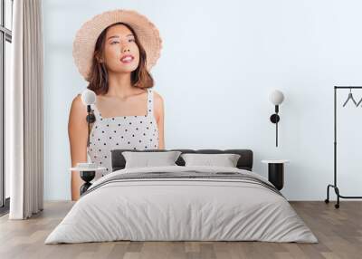 Young beautiful chinese girl wearing summer hat looking away to side with smile on face, natural expression. laughing confident. Wall mural