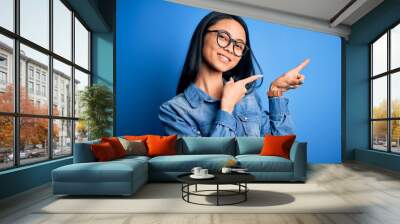 Young beautiful chinese woman wearing casual denim shirt over isolated blue background smiling and looking at the camera pointing with two hands and fingers to the side. Wall mural