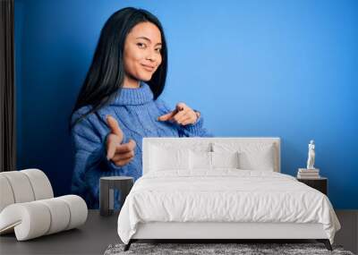 Young beautiful chinese woman wearing casual sweater over isolated blue background pointing fingers to camera with happy and funny face. Good energy and vibes. Wall mural