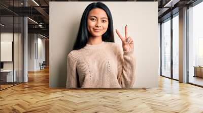 Young beautiful chinese woman wearing casual sweater over isolated white background showing and pointing up with fingers number two while smiling confident and happy. Wall mural