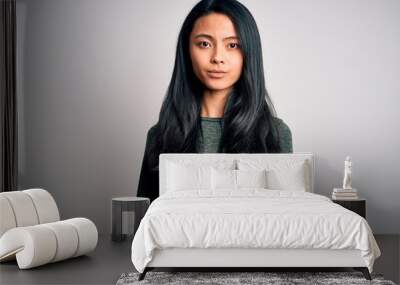 Young beautiful chinese woman wearing casual t-shirt over isolated white background with serious expression on face. Simple and natural looking at the camera. Wall mural