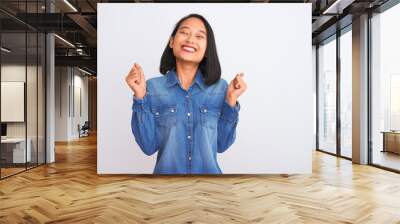 Young beautiful chinese woman wearing denim shirt standing over isolated white background excited for success with arms raised and eyes closed celebrating victory smiling. Winner concept. Wall mural