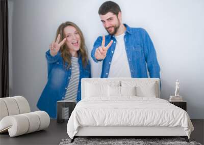 Young beautiful couple standing together over white isolated background smiling looking to the camera showing fingers doing victory sign. Number two. Wall mural