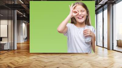 Young beautiful girl drinking glass of water over isolated background with happy face smiling doing ok sign with hand on eye looking through fingers Wall mural