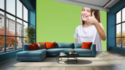 Young beautiful girl over isolated background doing happy thumbs up gesture with hand. Approving expression looking at the camera with showing success. Wall mural