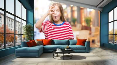 Young beautiful girl over isolated background doing ok gesture shocked with surprised face, eye looking through fingers. Unbelieving expression. Wall mural