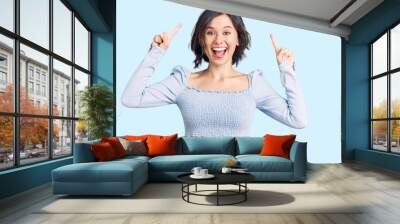 Young beautiful girl wearing casual clothes smiling amazed and surprised and pointing up with fingers and raised arms. Wall mural