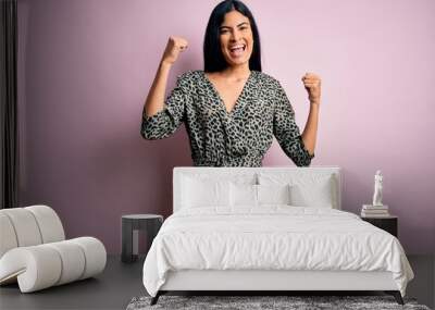 Young beautiful hispanic fashion woman wearing casual dress over pink background celebrating surprised and amazed for success with arms raised and open eyes. Winner concept. Wall mural