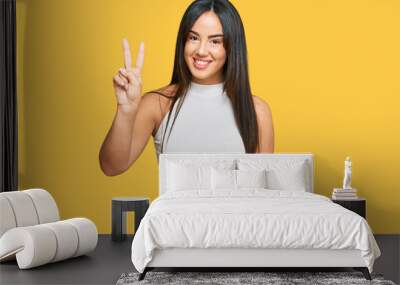 Young beautiful hispanic girl wearing casual clothes showing and pointing up with fingers number two while smiling confident and happy. Wall mural