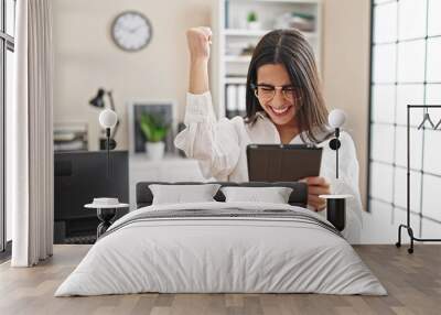 Young beautiful hispanic woman business worker using touchpad with winner expression at office Wall mural