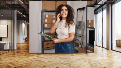 Young beautiful hispanic woman ecommerce business worker talking on smartphone reading document at office Wall mural