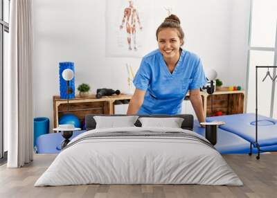 Young beautiful hispanic woman physiotherapist smiling confident standing at rehab clinic Wall mural