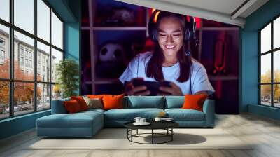 Young beautiful hispanic woman streamer playing video game using smartphone at gaming room Wall mural