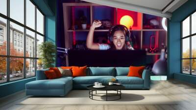 Young beautiful hispanic woman streamer playing video game with winner expression at gaming room Wall mural