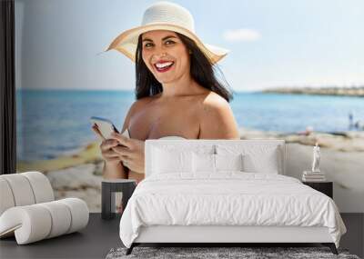 Young beautiful hispanic woman tourist smiling confident using smartphone at seaside Wall mural