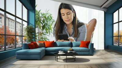 Young beautiful hispanic woman using smartphone wearing earphones at home Wall mural