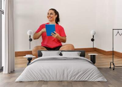 Young beautiful hispanic woman using touchpad sitting on floor at empty room Wall mural