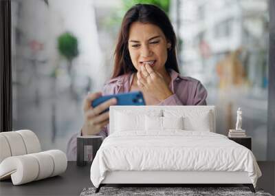 Young beautiful hispanic woman watching video on smartphone stressed at street Wall mural