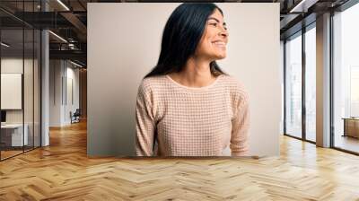 Young beautiful hispanic woman wearing elegant pink sweater over isolated background looking away to side with smile on face, natural expression. Laughing confident. Wall mural