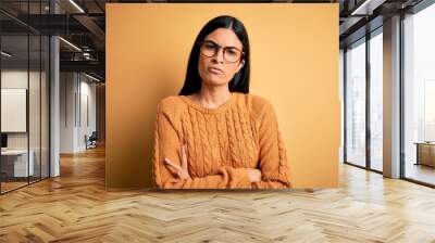 Young beautiful hispanic woman wearing glasses over yellow isolated background skeptic and nervous, disapproving expression on face with crossed arms. Negative person. Wall mural