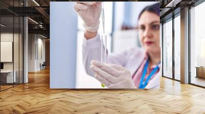 Young beautiful plus size woman scientist pouring liquid on test tube at laboratory Wall mural