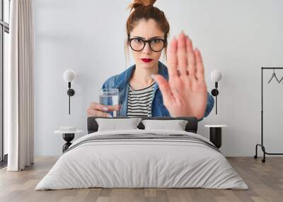 Young beautiful redhead woman drinking glass of water over isolated white background with open hand doing stop sign with serious and confident expression, defense gesture Wall mural