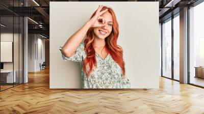 Young beautiful redhead woman wearing casual clothes smiling happy doing ok sign with hand on eye looking through fingers Wall mural