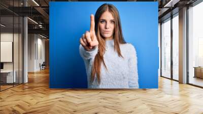 Young beautiful redhead woman wearing casual sweater over isolated blue background Pointing with finger up and angry expression, showing no gesture Wall mural