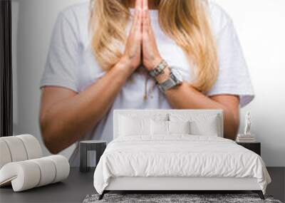 Young beautiful woman casual white t-shirt over isolated background praying with hands together asking for forgiveness smiling confident. Wall mural