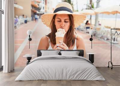 Young beautiful woman eating ice cream cone by the beach on a sunny day of summer on holidays Wall mural