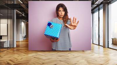 Young beautiful woman holding birthday gift over pink isolated background with open hand doing stop sign with serious and confident expression, defense gesture Wall mural