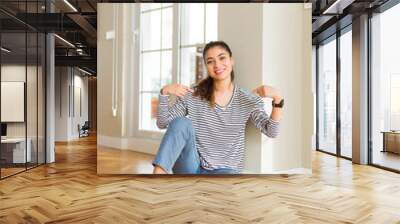 Young beautiful woman sitting on the floor at home looking confident with smile on face, pointing oneself with fingers proud and happy. Wall mural