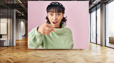 Young beautiful woman standing over pink background pointing with finger surprised ahead, open mouth amazed expression, something on the front Wall mural