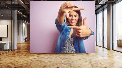 Young beautiful woman standing over pink isolated background smiling making frame with hands and fingers with happy face. Creativity and photography concept. Wall mural