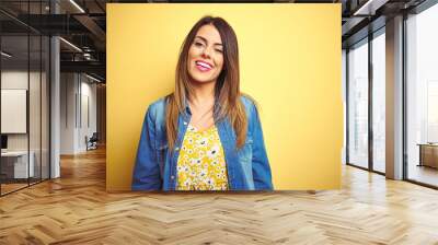 Young beautiful woman standing over yellow isolated background winking looking at the camera with sexy expression, cheerful and happy face. Wall mural