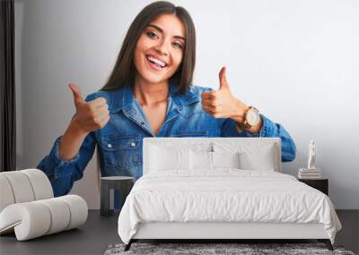 Young beautiful woman wearing casual denim shirt standing over isolated white background success sign doing positive gesture with hand, thumbs up smiling and happy. Cheerful expression Wall mural