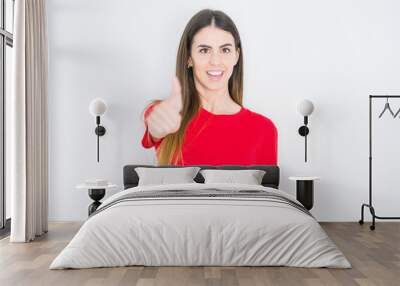 Young beautiful woman wearing casual red t-shirt over white isolated background doing happy thumbs up gesture with hand. Approving expression looking at the camera with showing success. Wall mural