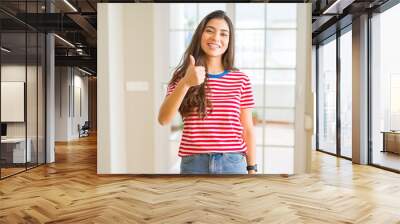 Young beautiful woman wearing casual t-shirt doing happy thumbs up gesture with hand. Approving expression looking at the camera showing success. Wall mural