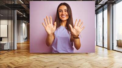 Young beautiful woman wearing casual t-shirt standing over isolated pink background showing and pointing up with fingers number ten while smiling confident and happy. Wall mural