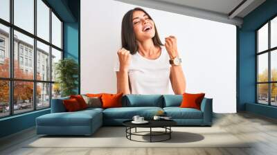 Young beautiful woman wearing casual t-shirt standing over isolated white background celebrating surprised and amazed for success with arms raised and eyes closed. Winner concept. Wall mural