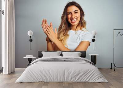 Young beautiful woman wearing casual white t-shirt over isolated background clapping and applauding happy and joyful, smiling proud hands together Wall mural