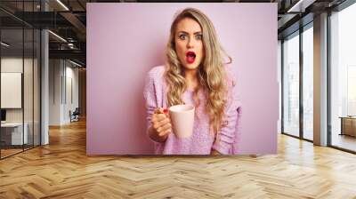 Young beautiful woman wearing sweater drinking a cup of coffee over pink isolated background scared in shock with a surprise face, afraid and excited with fear expression Wall mural